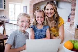 Portrait of mother and kids using laptop in kitchen