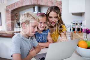 Mother and kids using laptop in kitchen