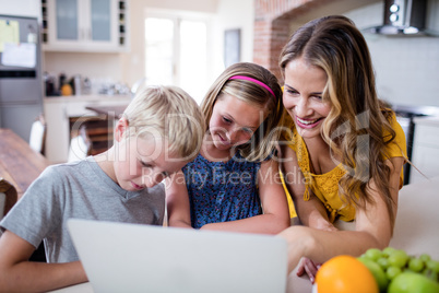 Mother and kids using laptop in kitchen