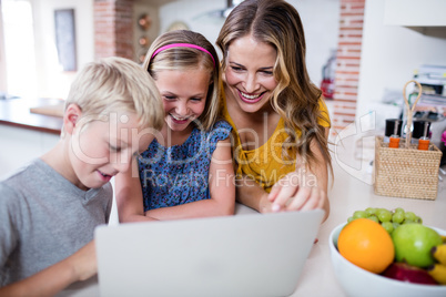 Mother and kids using laptop in kitchen