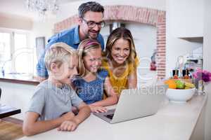 Parents and kids using laptop in kitchen