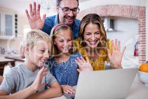 Parents and kids waving hands while using laptop for video chat
