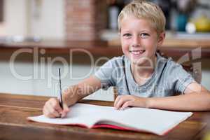 Portrait of happy boy doing homework in kitchen