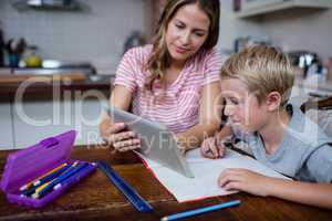 Mother using a digital tablet while helping son with his homewor