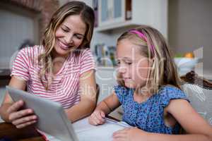 Mother using a digital tablet while helping daughter with her ho