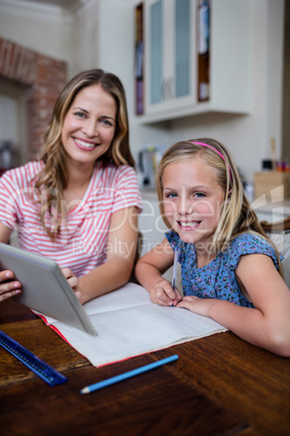 Mother using a digital tablet while helping daughter with her ho