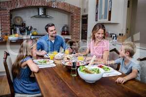 Happy family talking to each other while having meal in kitchen