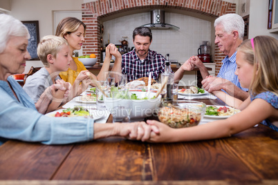 Multi-generation family praying before having meal