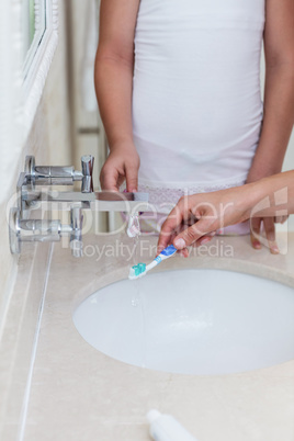 Mid section of mother and daughter washing their toothbrush in w