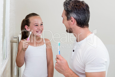 Smiling daughter and father holding a toothbrush in the bathroom