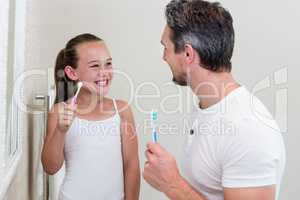 Smiling daughter and father holding a toothbrush in the bathroom