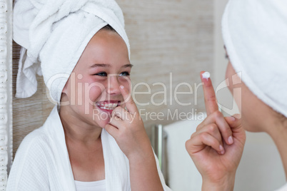 Smiling mother and daughter applying moisturizer on nose