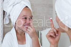 Smiling mother and daughter applying moisturizer on nose