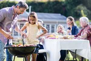 Father and daughter at barbecue grill while family having lunch