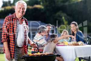 Senior man at barbecue grill while family having lunch in backgr