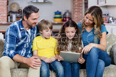 Parents and kids sitting on sofa and using a digital tablet