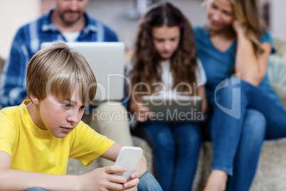 Boy using a mobile phone while family in background