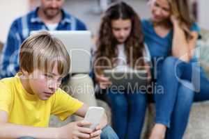 Boy using a mobile phone while family in background