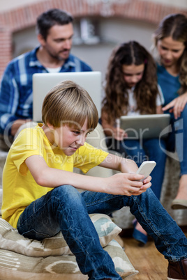 Boy using a mobile phone while family in background