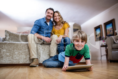 Boy using a digital tablet while parents sitting on sofa in back Boy using a digital tablet while parents sitting on sofa in back
