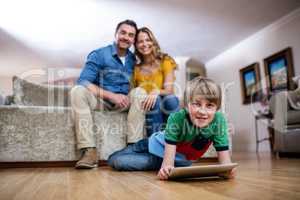 Boy using a digital tablet while parents sitting on sofa in back