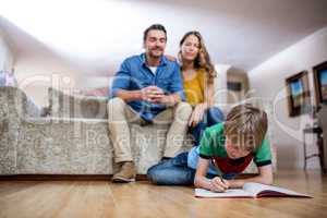 Boy doing homework while parents sitting on sofa in background