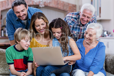 Multi-generation family sitting on sofa and using laptop