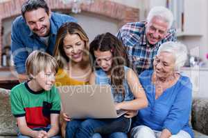 Multi-generation family sitting on sofa and using laptop
