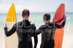Father and son with surfboard standing on beach