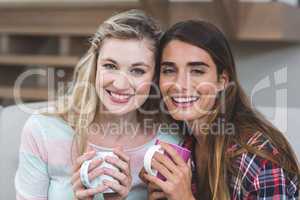 Two beautiful women sitting side by side with a mug of coffee