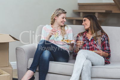 Two beautiful woman sitting on sofa and having pizza