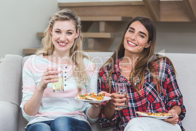 Two beautiful women sitting on sofa and having pizza