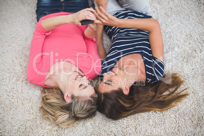 Two beautiful women lying on rug looking at the mobile phone