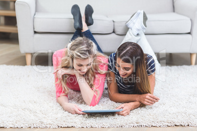 Two beautiful women lying on rug and using digital tablet