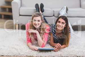 Two beautiful women lying on rug and using digital tablet