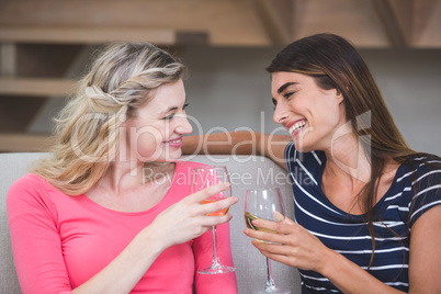Two beautiful women holding glass of wine and talking in the liv