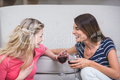 Two beautiful women holding glass of wine and talking in the liv