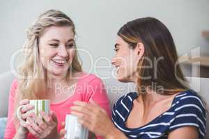 Two beautiful women holding a cup of coffee and talking in the l