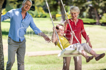 Grandparents pushing their granddaughter on swing