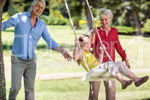 Grandparents pushing their granddaughter on swing