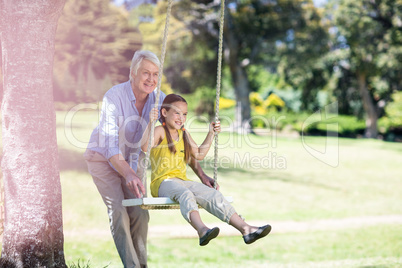 Grandfather pushing his granddaughter on swing