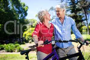 Senior couple standing with bicycle in park