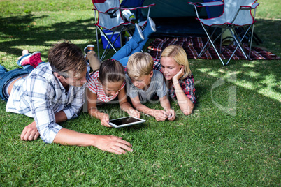 Family lying on grass and using digital tablet