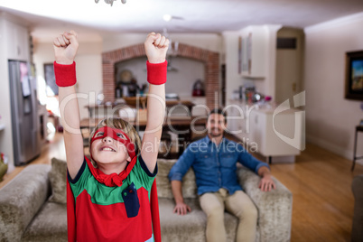 Son pretending to be a superhero while father sitting on sofa