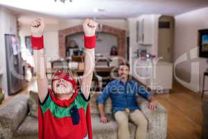 Son pretending to be a superhero while father sitting on sofa