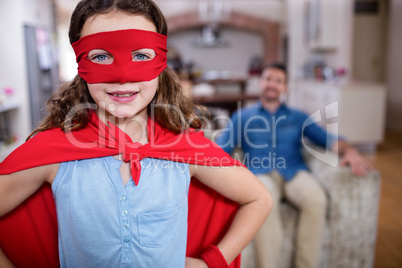 Daughter pretending to be a superhero while father sitting on so