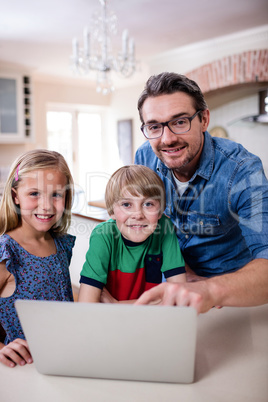 Portrait of father and kids using laptop in kitchen