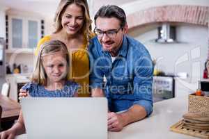 Parents and daughter using laptop in kitchen