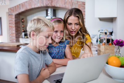 Mother and kids using laptop in kitchen