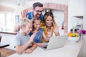 Parents and kids waving hands while using laptop for video chat